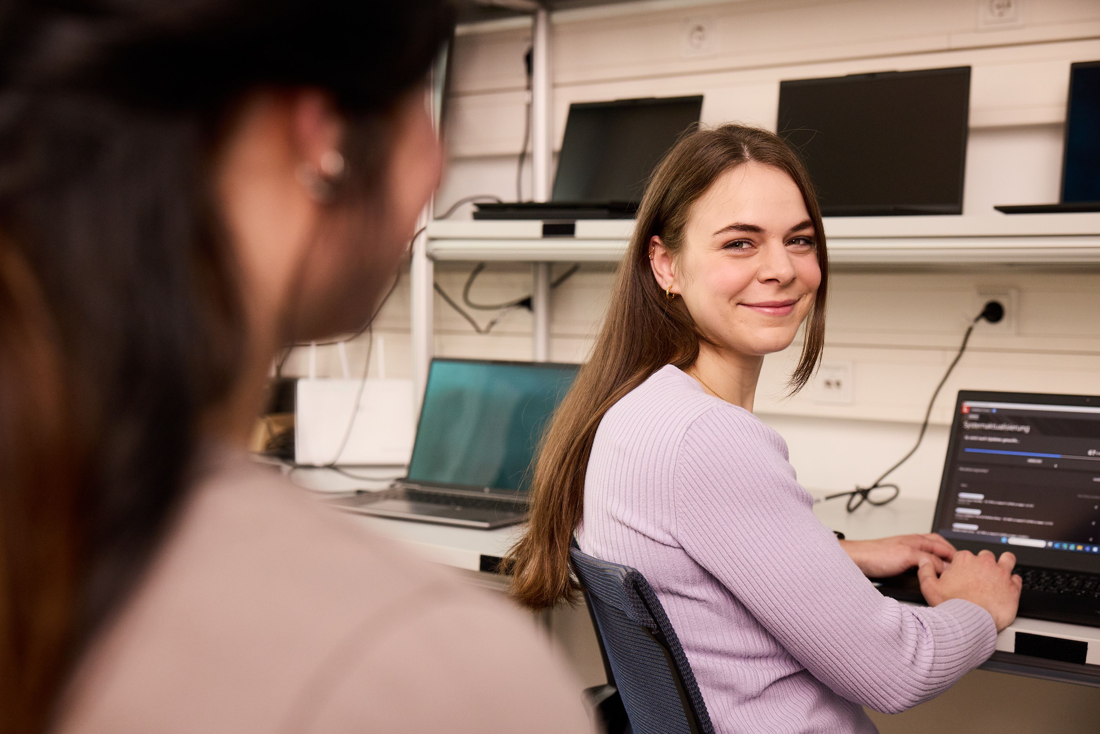 IT-Administratorin sitzt vor aufgeklapptem Laptop und lächelt in die Kamera