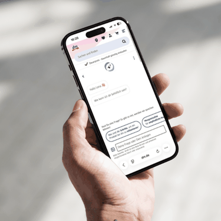 Eine Hand hält ein Smartphone auf dem der digitale Assistent dmKI im dm Onlineshop geöffnet ist